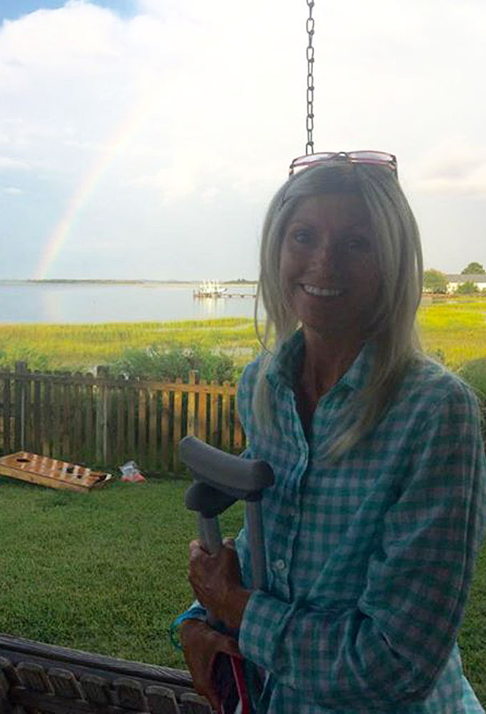 Rhonda, a woman holding a pair of crutches outside.  A rainbow is in the background.