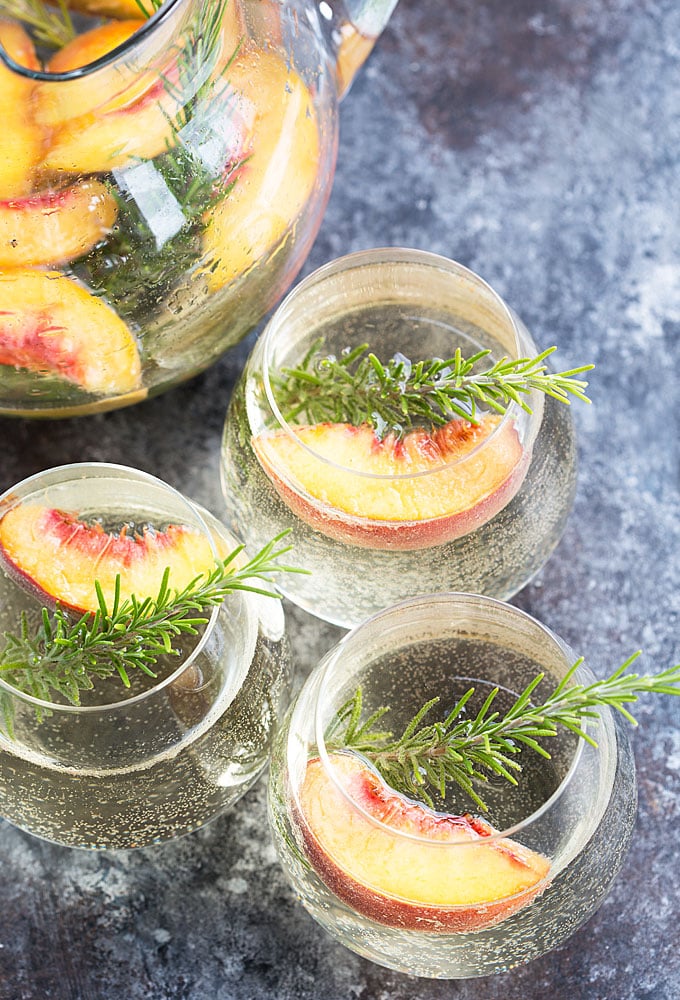 Overhead view of white peach sangria with rosemary in three glasses.