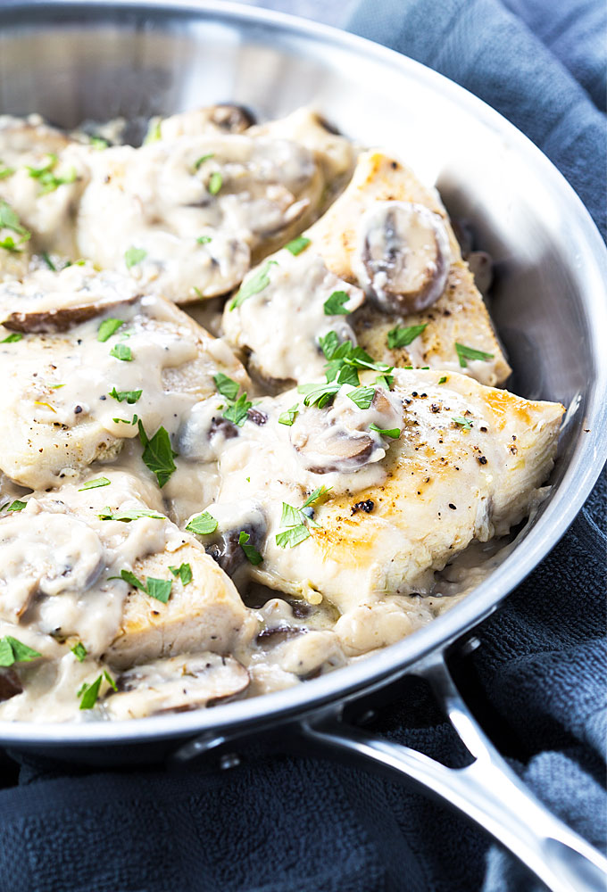Chicken in a creamy garlic mushroom sauce in a stainless skillet by a towel.