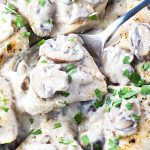A closeup of a large spoon holding chicken topped with a mushroom cream sauce.