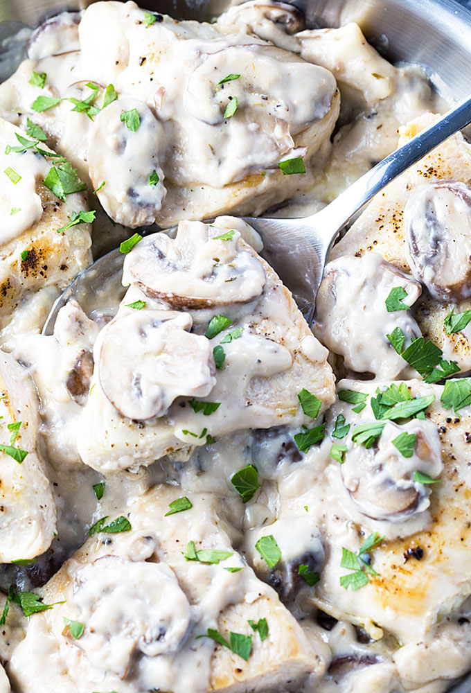 A large spoon holding a piece of chicken topped with a mushroom cream sauce.