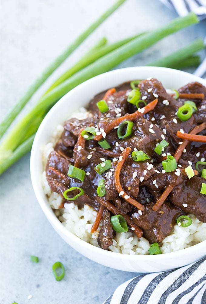 Overhead view of slow cooker Mongolian beef over rice in a white bowl.