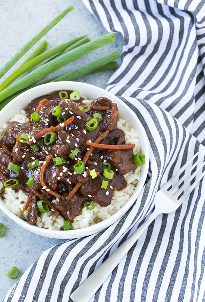 Overhead view of Mongolian beef over rice in a white bowl.