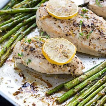 Baked boneless chicken breasts and asparagus spears on a baking sheet.