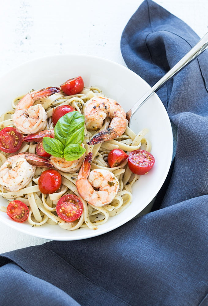 Overhead view of buttery shrimp over pesto pasta with tomatoes in a white bowl.