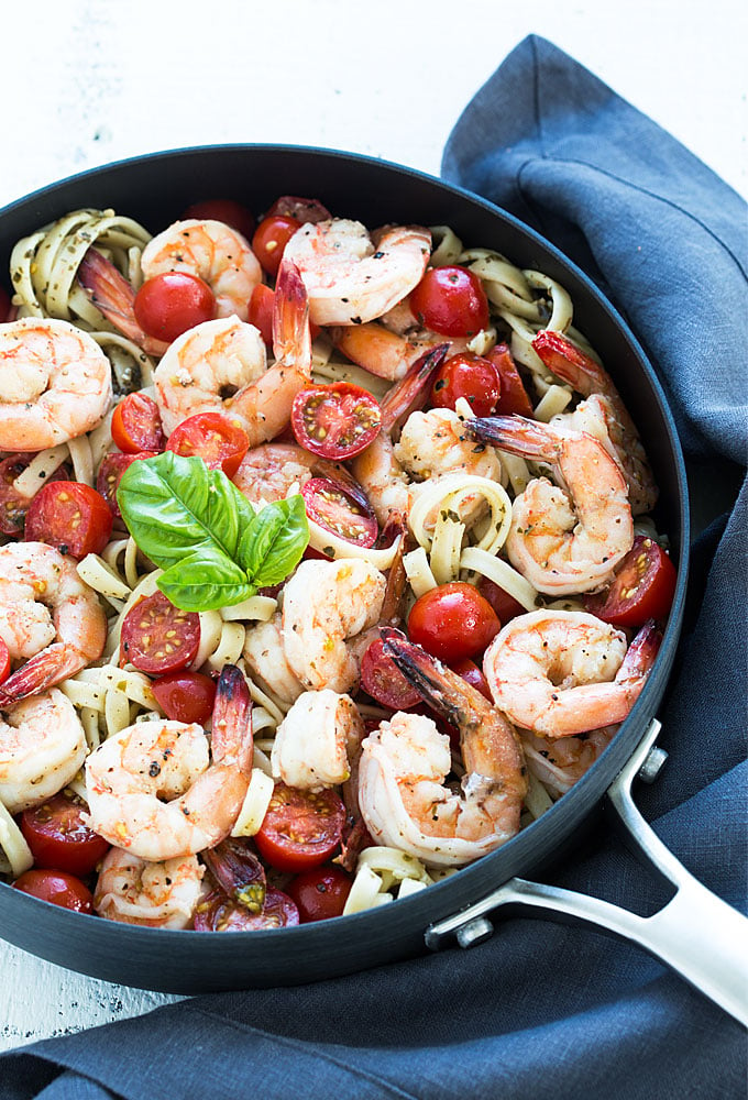 Overhead view of shrimp with pesto pasta and cherry tomatoes in a skillet.