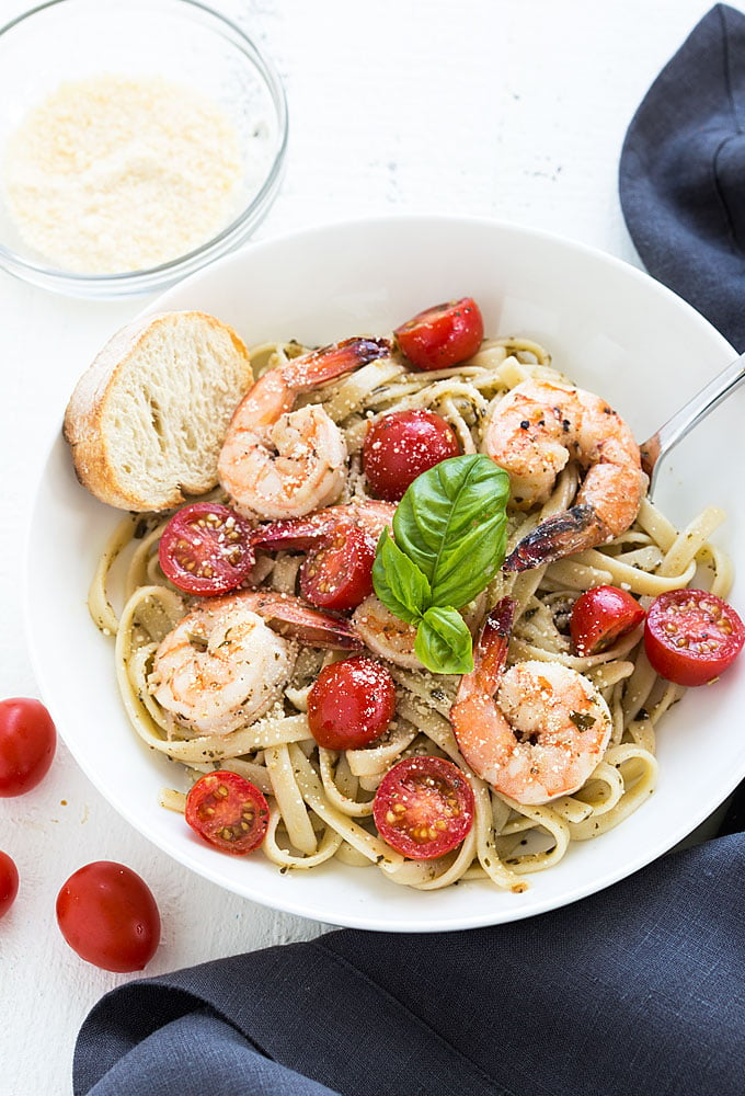 Overhead view of buttery shrimp with pesto pasta and tomatoes in a white bowl.
