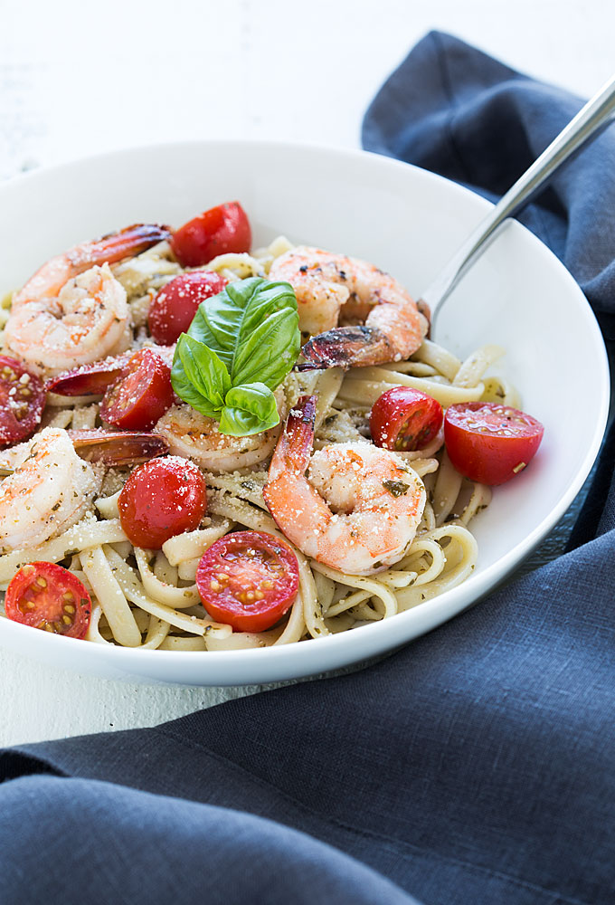 Pasta topped with shrimp, tomatoes and fresh basil in a white bowl.