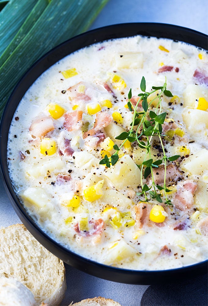 Overhead closeup of corn chowder topped with fresh thyme sprigs in a black bowl.
