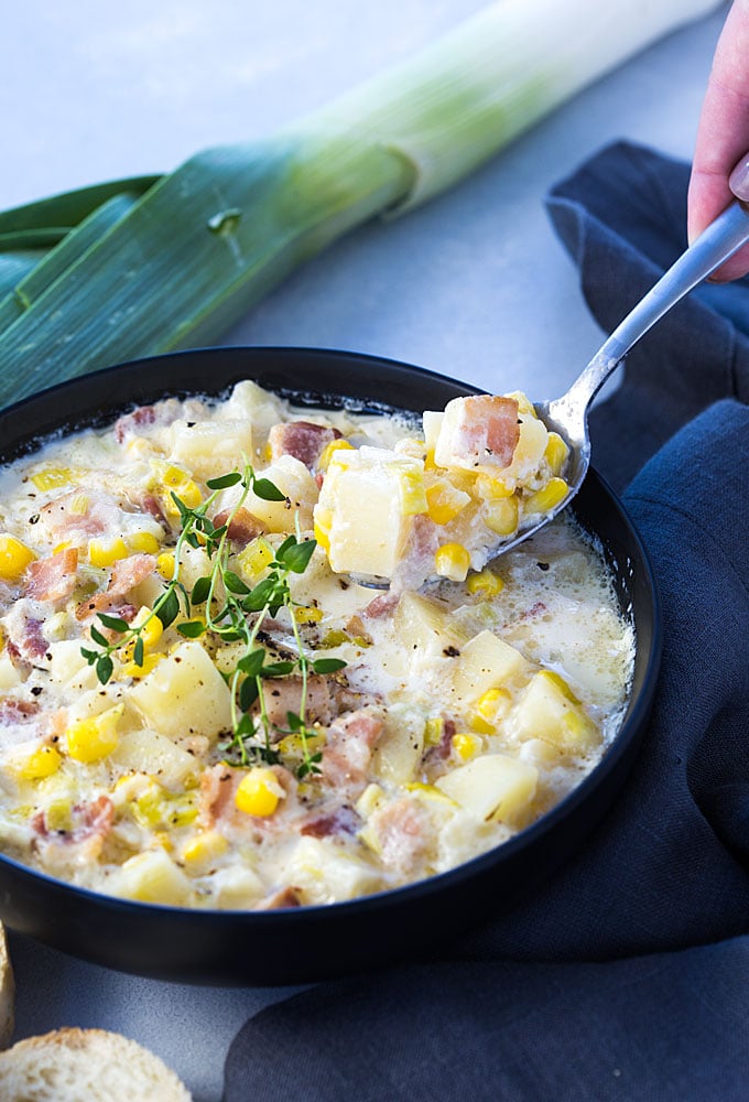 A spoon spooning corn chowder from a black bowl.