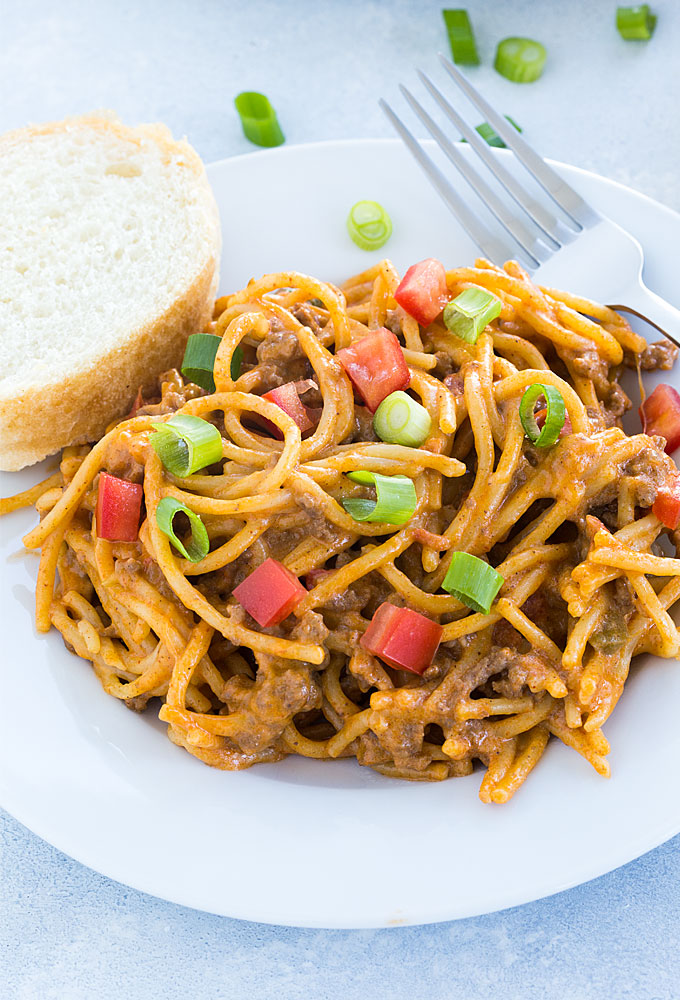 Creamy taco spaghetti on a white plate with a fork and slice of French bread.