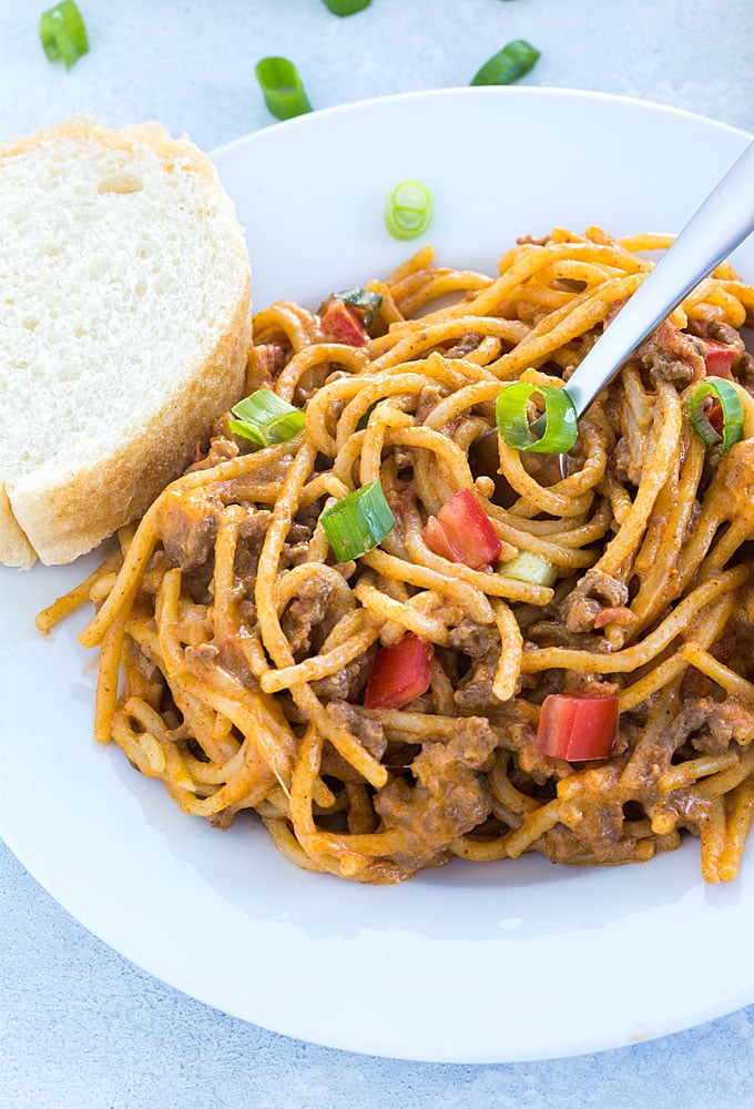 A closeup view of taco spaghetti on a white plate with a piece of French bread.