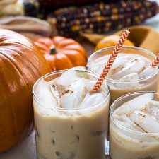 Three glasses of white russians by decorative pumpkins.