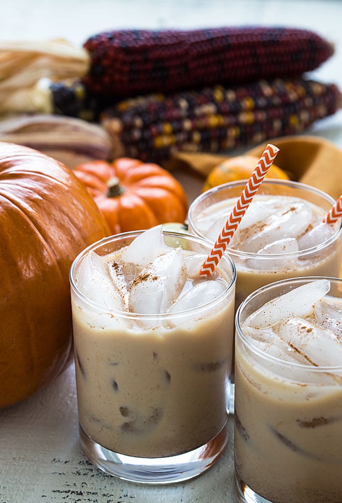 Three glasses of white russians by decorative pumpkins.