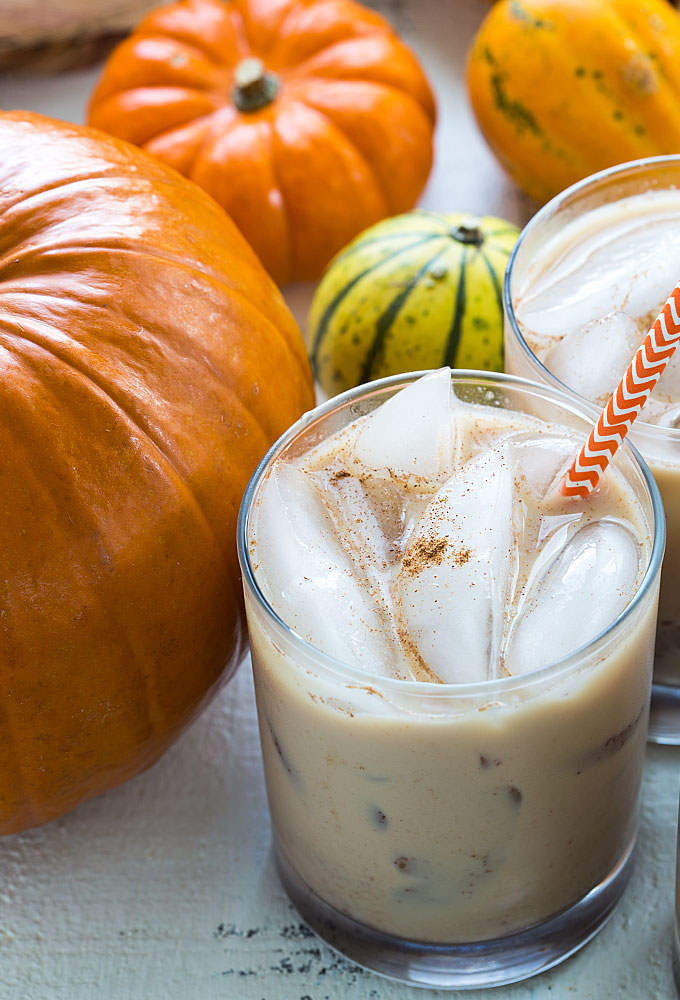 A closeup of a glass of white russian cocktail by a pumpkin.