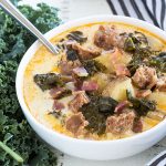 A white bowl of zuppa toscana by fresh kale and a striped napkin.
