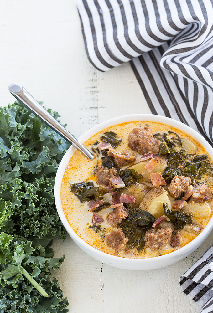 Overhead view of a bowl of zuppa toscana by fresh kale and a striped napkin.