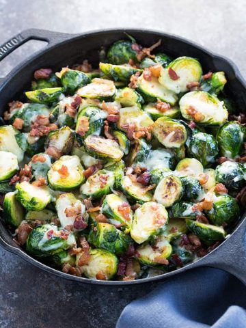 Baked brussels sprouts with cheese and bacon in a cast iron skillet.