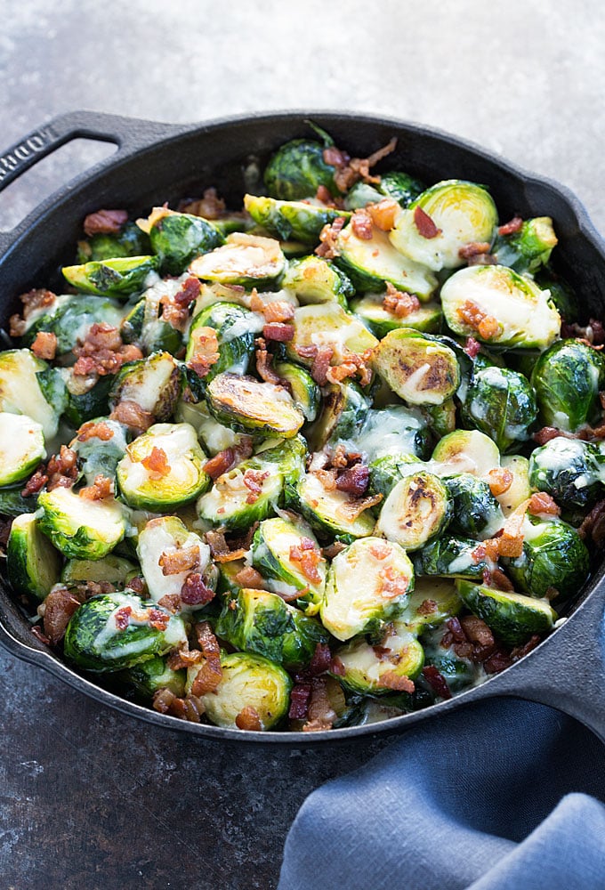 Baked brussels sprouts with cheese and bacon in a cast iron skillet.