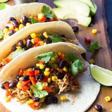 Three chicken and black bean tacos with cilantro on a wooden cutting board.