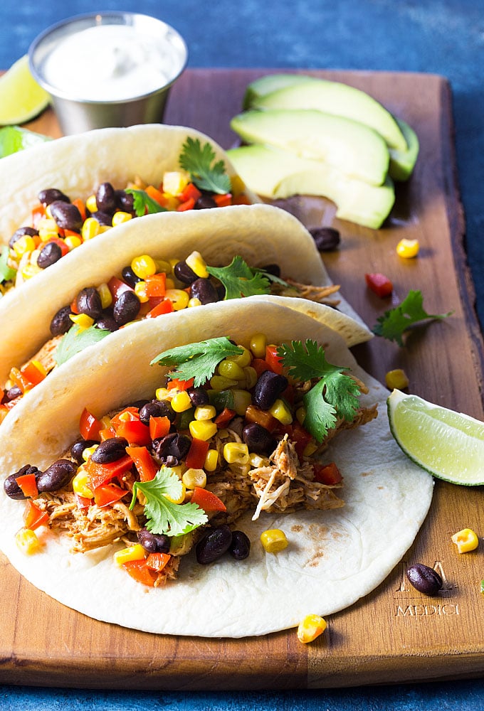 Three chicken and black bean tacos with cilantro on a wooden cutting board.