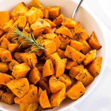 Roasted bite size pieces of sweet potatoes with rosemary in a white bowl.