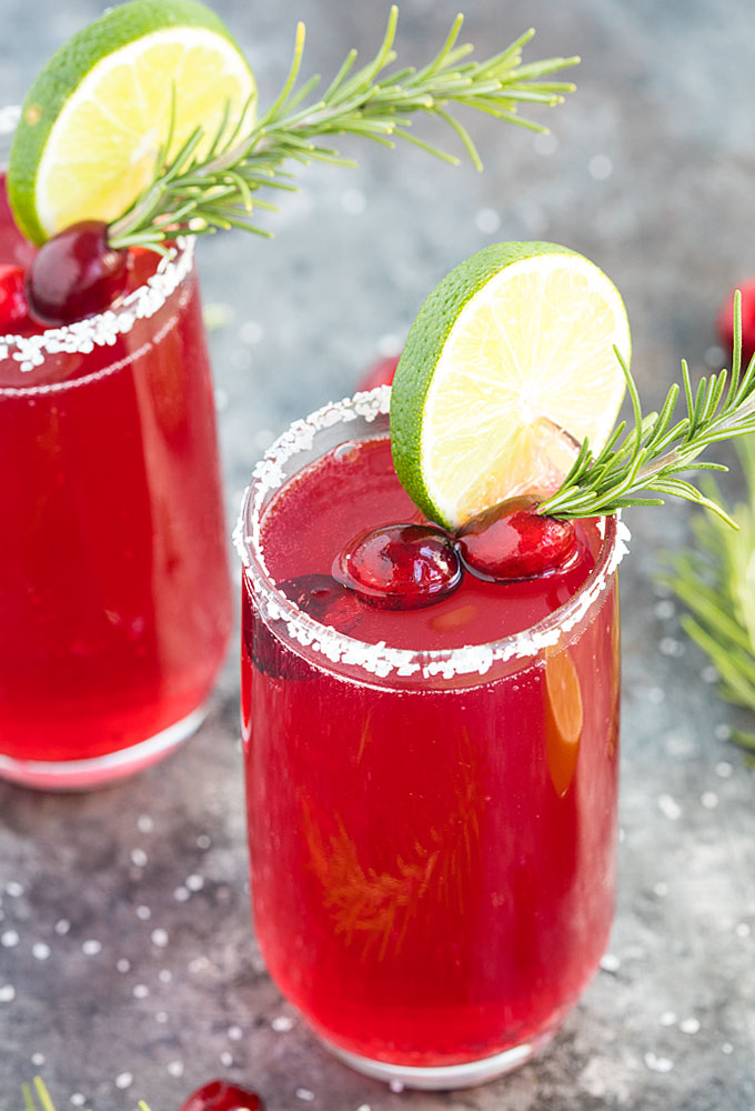 Closeup view of a cranberry mimosa margarita with cranberries, lime and rosemary.