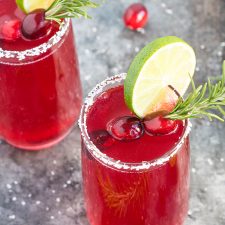 Overhead view of two cranberry cocktails garnished with lime, cranberries and rosemary.