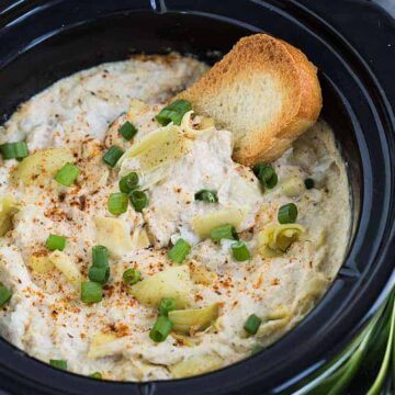 A piece of French bread dipped into artichoke crab dip in a slow cooker.