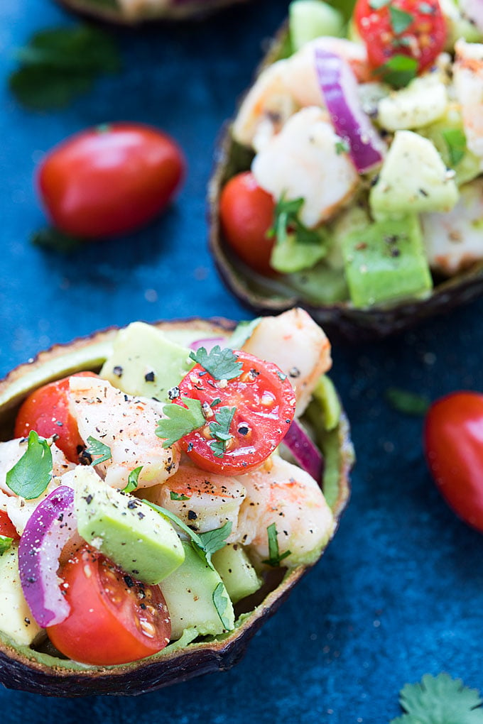 A closeup of a halved avocado shell filled with shrimp and vegetables.
