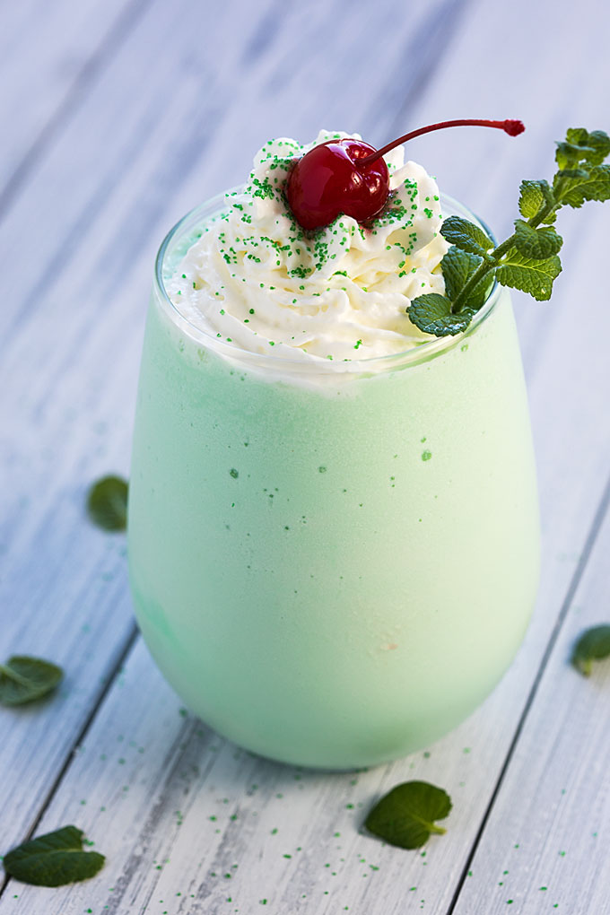 Front view of a mint shamrock shake with vodka on a white wood surface.