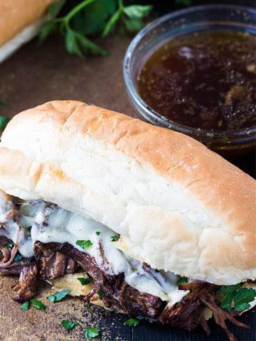 A closeup of a French dip sandwich beside a bowl of au jus.