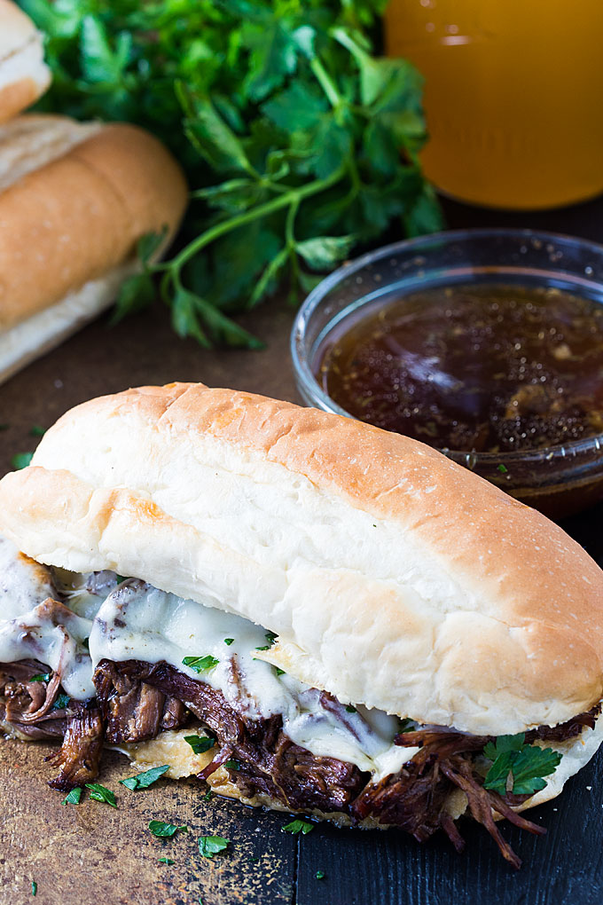 A French dip sandwich beside parsley and a bowl of au jus.