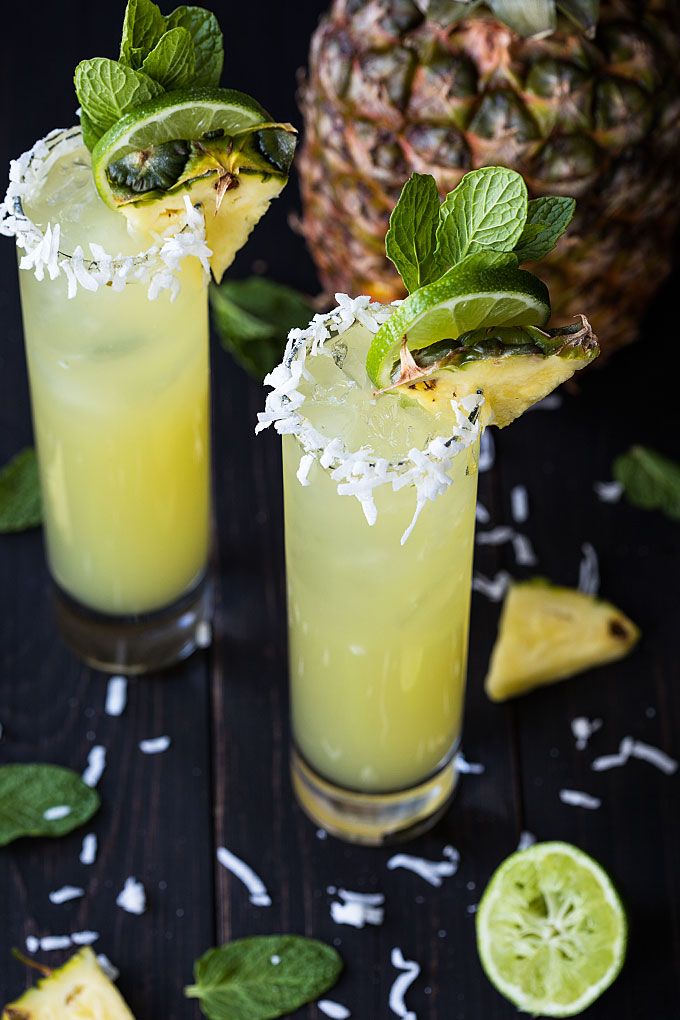Two pineapple coconut mojitos on a dark surface.