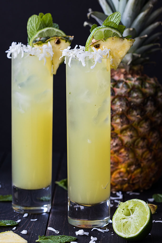 Front view of two pineapple coconut mojitos.  A pineapple is in the background.