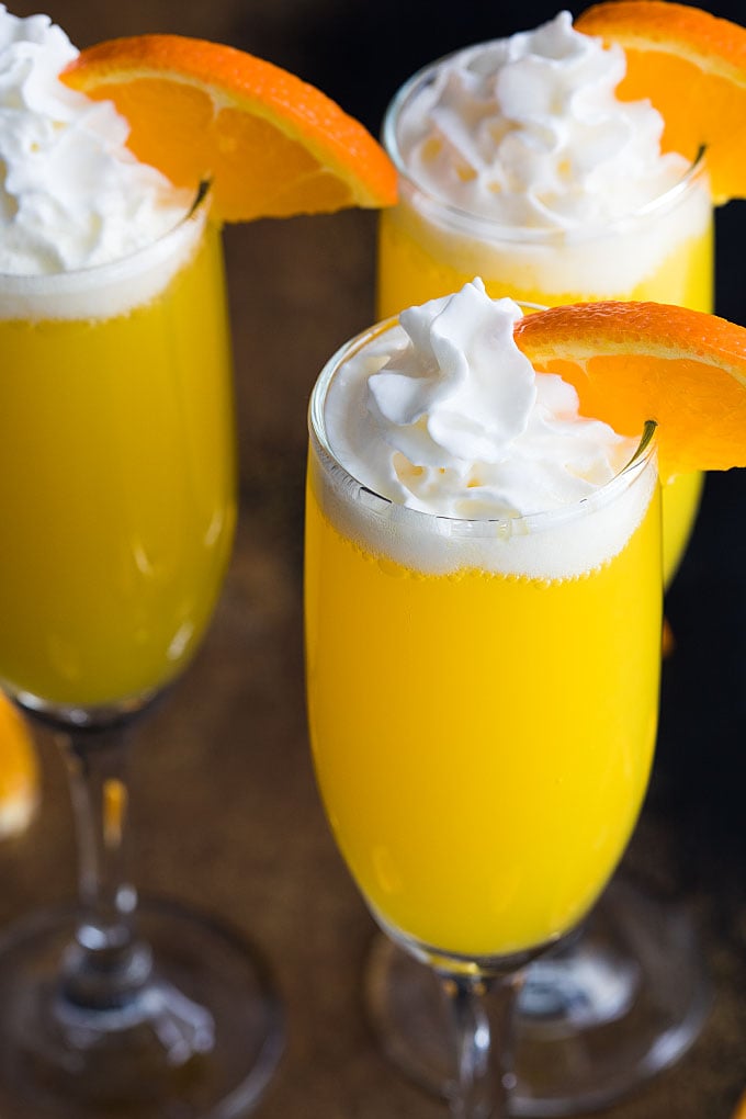 Three creamsicle mimosas with whipped topping and an orange slice in champagne flutes.