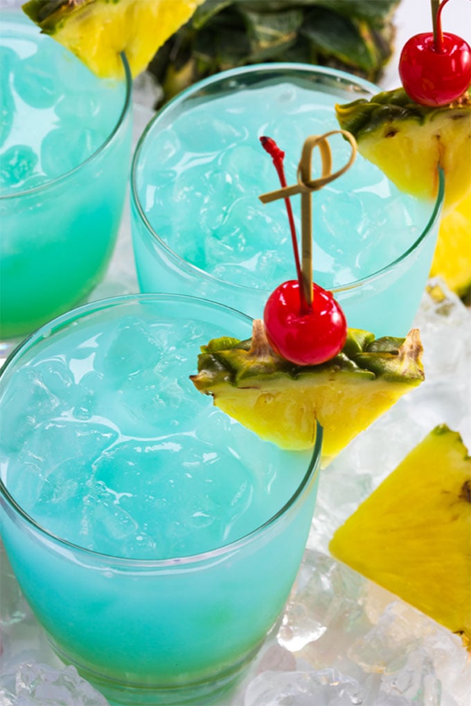 Overhead view of three bluewater breeze cocktails garnished with pineapple and cherries.