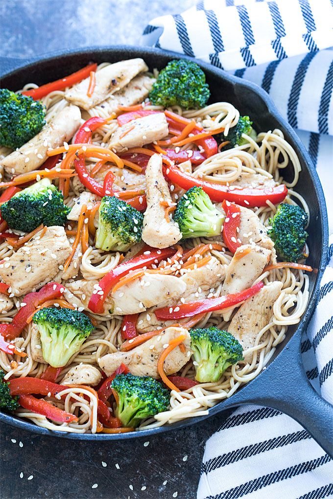 Chicken and broccoli lo mein in a cast iron skillet beside a striped napkin.