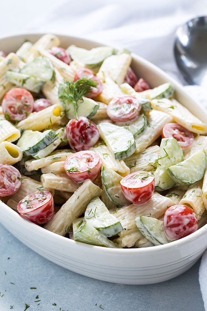 Front closeup view of creamy cucumber and tomato pasta salad in an oval white dish.