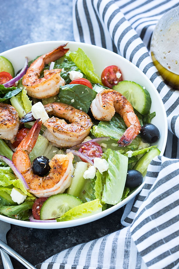 A closeup overhead view of Greek salad with shrimp in a white bowl.