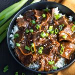 Overhead view of Mongolian beef over rice in a black bowl.