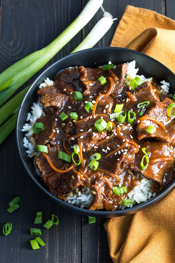 Overhead view of Mongolian beef over rice in a black bowl.