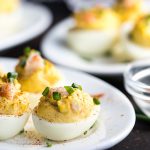 A closeup view of deviled eggs with shrimp on an oval white plate.
