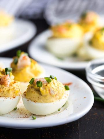 A closeup view of deviled eggs with shrimp on an oval white plate.