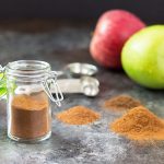 Spice in a spice jar.  Apples and a set of measuring spoons are in the background.
