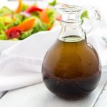 A bottle of balsamic vinaigrette with a salad in the background.