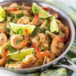 Shrimp with pasta topped with lime wedges and chopped cilantro in a skillet.