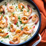 Overhead view of pasta in Alfredo sauce with seasoned shrimp in a skillet.