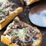A slice of French bread pizza with mushrooms by a pizza cutter.