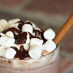 A closeup of hot chocolate cocktail in a mug topped with marshmallows and chocolate syrup.